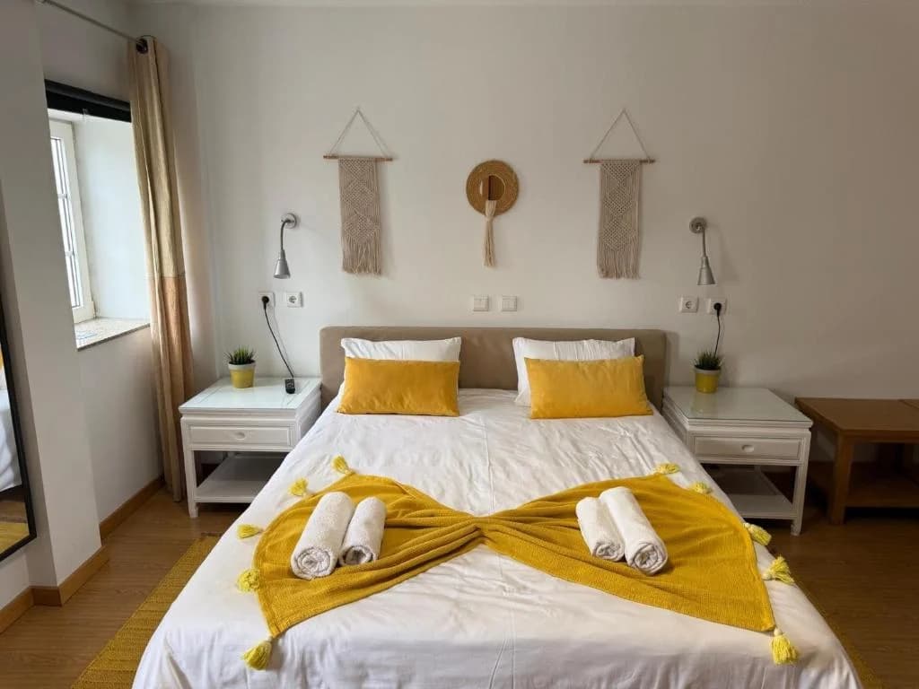 Quarto Citrino na Casa Miná com cama de casal, roupa de cama branca e detalhes amarelos, ambiente acolhedor