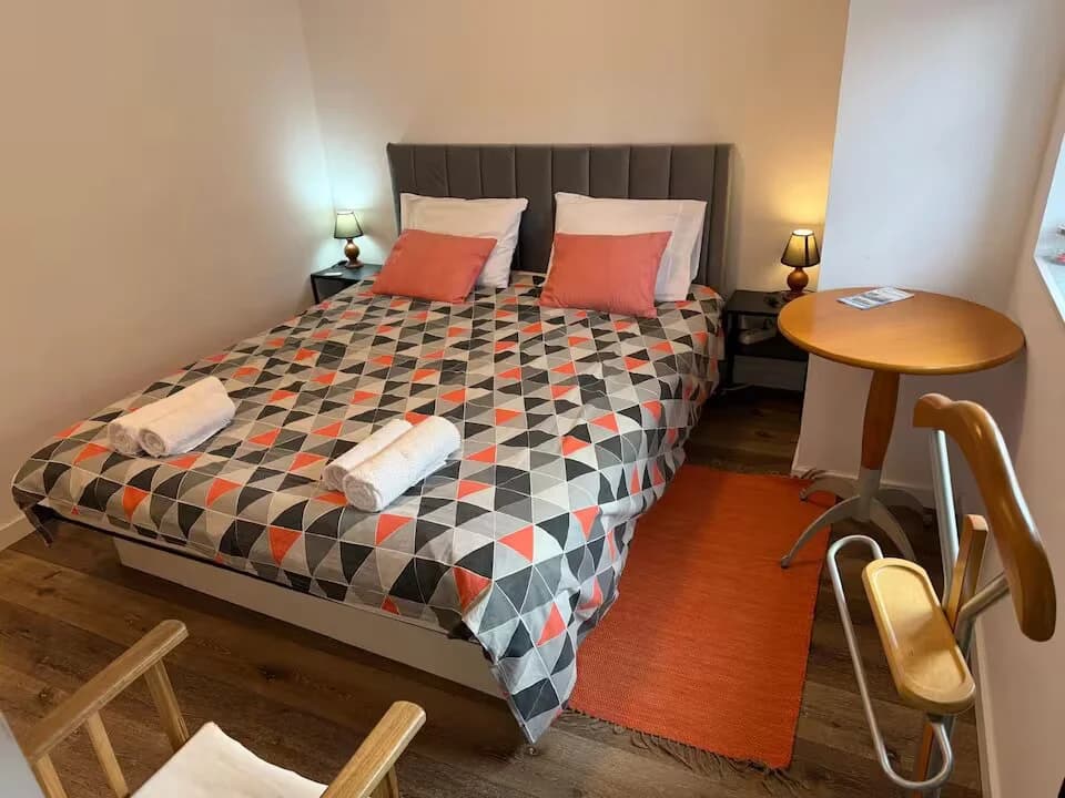 Quarto com cama de casal, almofadas decorativas e mesa lateral junto à janela