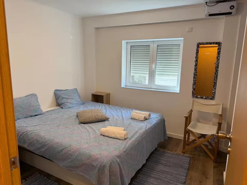 Quarto Sodalita com cama de casal, decoração simples, janela e ar condicionado na parede